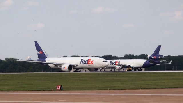 BOEING 777-200LR (N856FD) - "Shae" taxis to 36C as N585FE "Katherine" begins her takeoff roll down 36R. 