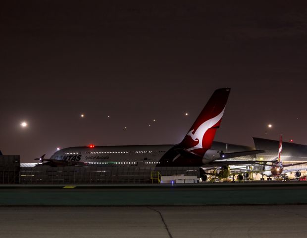 Airbus A380-800 (VH-OQK) - Hopping around Los Angeles International (LAX) at night-This big A380 has been moved out of the hangar and is being towed to the gates for its next departure. Qantas is an acronym which means Queensland and Northern Territory Aerial Services and is the worlds oldest airline, founded in 1920 in Winton, Australia. Another Qantas A380 can be seen at the terminal to the right. A US Airways A321 is parked in the middle. The sky is still full of arrivals coming in for westerly landings on runways 24R and L. Photo taken at 21:22 22 Aug 13.