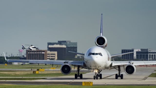 Boeing MD-11 (N615FE) - Taxiing to depart 13R while a helicopter approaches to land in the background