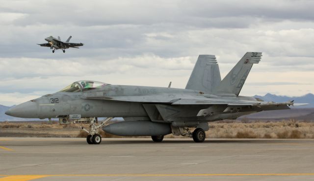 16-6818 — - Lt. Pete "Smelly Cat" Daniels holds his F/A-18E Super Hornet, assigned to the Strike Fighter Squadron 136 (VFA 136) "Knighthawks" and homeported at NAS Oceana, on taxiway Bravo at Naval Air Station Fallon as another F/A-18E Super Bug (166954, assigned to the VFA 86 "Sidewinders" and piloted by LCDR R.G. "Fleadip" Bieze) glides toward NFLs runway 31L.  Lt Daniels was taking off to participate in a Top Gun training mission while LCDR Bieze was returning from a just-completed TG sortie.  (I wish the day had been sunny, but Id have stood in the rain for this photo opportunity.)