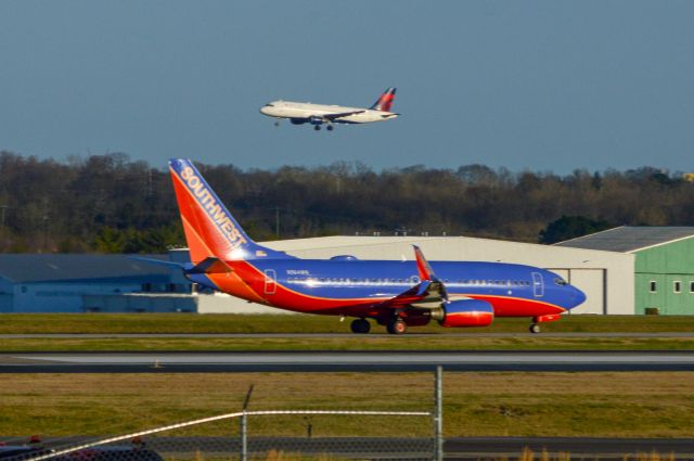 Boeing 737-700 (N964WN) - N964WN is taxing to the active during golden hour here at Nashville.  This was Southwest 32 departing for Chicago Midway while a Delta A320 as flight 2182 lands in the background on 2R from Detroit.  This shot was taken at 6:06 PM CDT with a Nikon D3200 at 200mm.