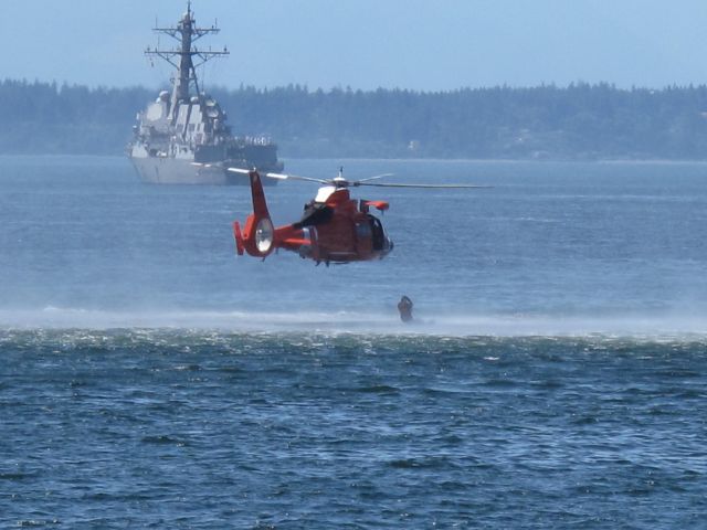 — — - US Coast Guard H-65 Dolphin helicopter in low hover, in order to deploy diver, for rescue demonstration in Seattles Elliott Bay during 2011 Seafair Fleet Week