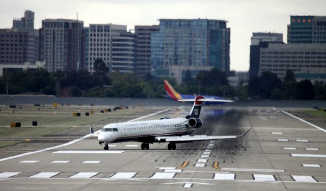 Canadair Regional Jet CRJ-900 (N247LR) - Mesa (American) #5739, turns East toward Terminal A, off of 30R, following arrival from KLAX as Southwest lines up for departure, City of San Jose skyline in background  07-07-2015