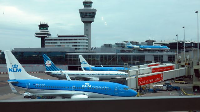 Boeing 737-700 (PH-BXA) - Commemorating 95 years KLM: Boeing 737 PH-BXA "Swan" in nostalgic company color house style design, standing at pier D between colleague 737s PH-BGD and PH-BGI at Schiphol Airport, Amsterdam. At the backgrounbd, decommisioned PH-OFE Fokker 100 cityhopper stands on permanent display on top of the  roof of the public view platform on the roof of the passenger terminal. 