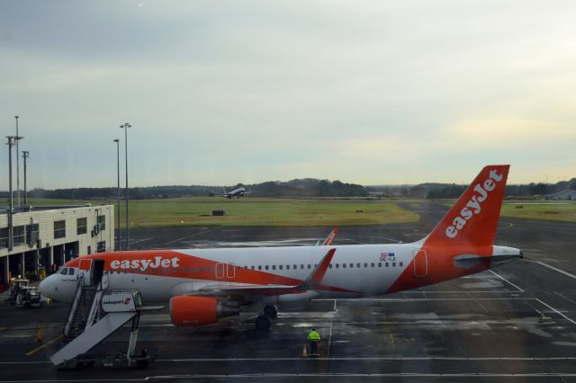 Airbus A320 (OE-IJI) - easyJet - A320-214WL (OE-IJI) on "stand" at NCL mid morning with a British Airways A321-251NX (G-NEOU) on "take off" in the background. Photo taken from inside NCL's "International Departures". Photo shows the odd "mark(s)" on windows overlooking the apron. (Photo 16 Oct 23)