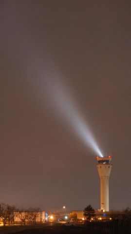 — — - The tower beacon shines through the dense fog and rain.