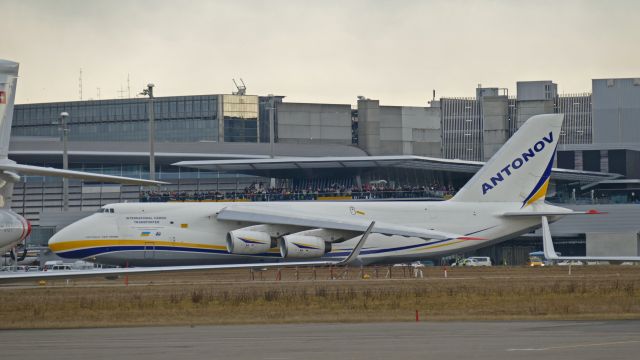 Antonov An-12 (UR-82007) - The terrace is crowded with spectators when the cargo plane passes just in front of them.