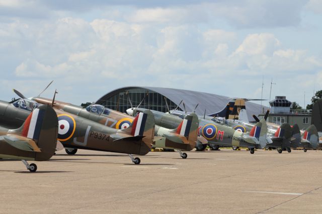 — — - A variety of Supermarine Spitfires on the flightline at Duxford Air Museum, with the American Air Museum Hangar in the background.