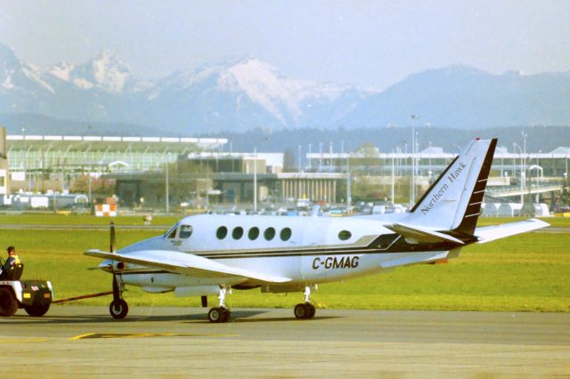 Beechcraft King Air 100 (C-GMAG) - CYVR - April 2004, I was up for the Vancouver Airline Collectible show near the airport, and decided to head out to the southern old terminal area and snap a few pictures with the Coast Range of the Canadian Rockies in the background. Beach 100 King Air for Northern Hawk aviation being towed to the ramp. There was also a Northern Hawk Dash 7 to the left of this view - editing that one later.