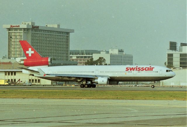 Boeing MD-11 (HB-IWC) - KLAX - early 1999 shows -IWC rolling to 25R for departure on this late afternoon flight for Zurich. This was a great location as we also had 25L traffic screaming overhead as 25R traffic idled up to the hold bars. There were 2 pesky lighted pole locations that were in the way but with proper lens alignment one could get decent photos here.