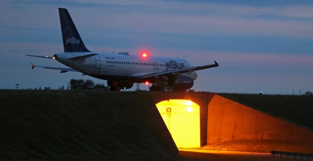 Airbus A320 (N508JL) - After an RON stay, JBU's "May The Force Be With Blue" (N508JL) is one of the first morning departures. Seen here as it passes over the first of two underpasses that run beneath Alpha Taxiway and Runway 23, jetBlue's early dawn departure was about to begin a flight from Buffalo to Fort Lauderdale (KFLL).