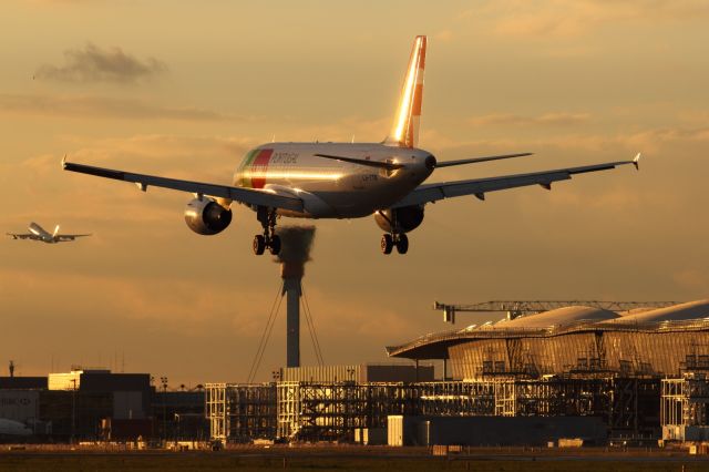 — — - A TAP Portagul A320-200 lands on runway 027L as a B747-400 takes off on runway 027R. In the background can be seen Terminal 2 still under construction at London Heathrow.