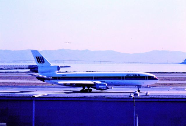 McDonnell Douglas DC-10 (N1834U) - KSFO - date apprx early to mid 1990s before the SFO Airport expansion, and eventual blocking this view, I used to park on the top floor of the inside garage area because I could park where I am shown here and see all of the 28LR arrivals and watch the 1LR departures, even though a bad sun angle. This DC-10 was leased from United new to Delta Airlines as N602DA and returned a few years later and re-reg to the N1834U United reg.here. The DC10 was on taxi the long way around the airport taxiways to Runway 28L left behind the tail, for departure most likely Honolulu. For the detailed oriented, I think the 727 on final is Western Airlines.