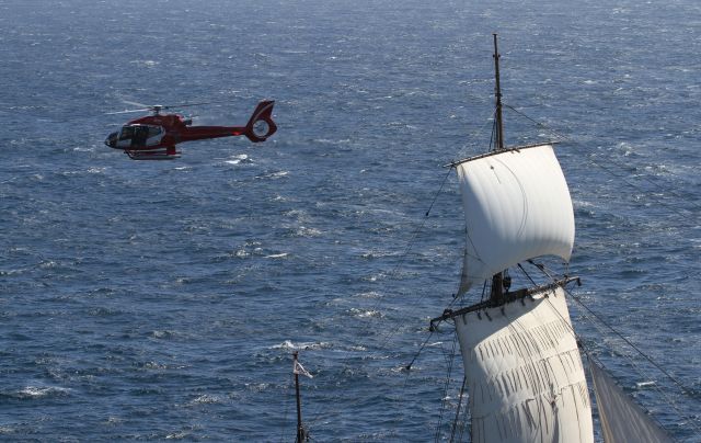— — - Taken from the top deck of Queen Mary 2 with the Endeavour under full sail. Both ships were on their circumnavigation of Australia 2012.The helicopter was was on a photo shoot for the occasion. See the web for further photos