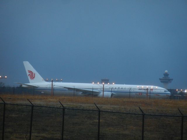 BOEING 777-300ER (B-2089) - An Air China Boeing B777-300ER Holds Short Of The Runway, B-2089 Had To Hold Short For About 15 Minutes While Waiting For Many Lightweights To Finish Landing, Dulles's Newest Air Traffic Control Tower Is In The Distance In Front Of B-2089, And Right Overtop Of B-2089 Is Dulles's Old Air Traffic Control Tower, which Is Not In Use And Is Probably Just Used As A Backup