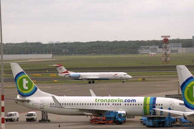 Boeing 737-800 (PH-HZE) - Transavia - B737-8K2 (PH-HZE) on "stand" at AMS with Austrian Arrows Fokker 100 (OE-LVI) taxiing in the background. (Photo May 2007)