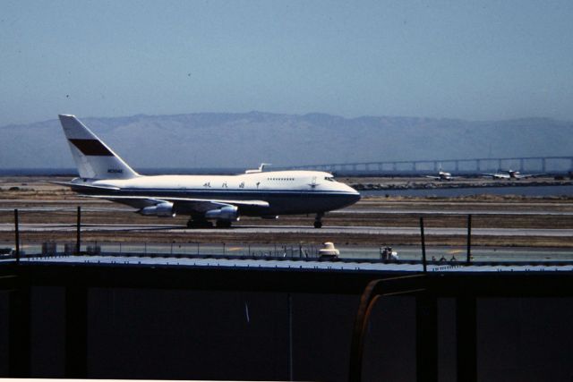 BOEING 747SP (N1304E) - SFO - daily visitor to KSFO back in this late 80s view. Note the DC-8 holding short on the 28L/R runways in the background with the San Mateo bridge visible on this fairly clear day.