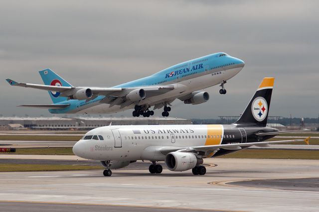 — — - A Korean Air B747-400 takes off as an US Airways A319 taxis to the gate. From South parking deck, H-J Atlanta International Airport.