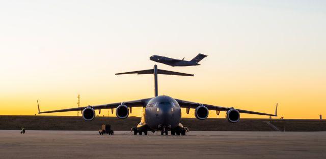 — — - A C-17 takes off while another rests on the ramp.