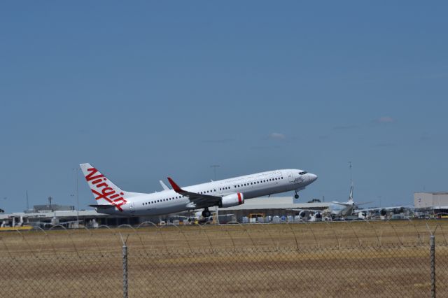 Boeing 737-800 (VH-YIJ) - Virgin 737-800 lifts off with a Cathay 747-8F unloading at the ramp.