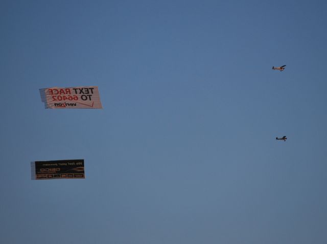 — — - VAN WAGNER AERIAL MEDIA LLC / Returning back to the airport from pre-race festivities at Charlotte Motor Speedway carrying the Verizon banner w/N8574C carrying the Geico banner. - 10/16/10
