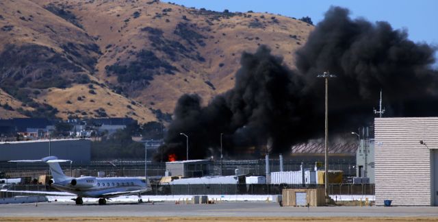 Gulfstream Aerospace Gulfstream G650 (N311CG) - Obviously a photo taken from across both runways and a taxiway, this fire broke out quite suddenly over by the cargo area at SFO. The Gulfstream (N311CG) was not in any immediate danger but when this pic was taken no emergency equipment had arrived at the scene yet, and we were wondering if it would be tugged to a different location. In my very next series of photos, the first fire truck to arrive on scene, San Francisco International Airport Truck 11, was passing behind the Gulfstream. I continued taking photos as more SFO fire units arrived and a short time later a City of San Francisco fire truck passed right by us as it arrived from the city. Within about fifteen minutes the fire was under control. The Gulfstream remained parked as seen here.