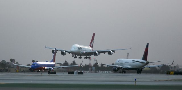 Airbus A380-800 (VH-OQK) - Action at LAX! This big QANTAS Airbus A380 is landing on runway 24 Right as a Southwest B737 takes off on runway 24 Left. The Delta plane is on the taxiway. Photo taken at 06:29 am on an overcast morning, Los Angeles, California USA