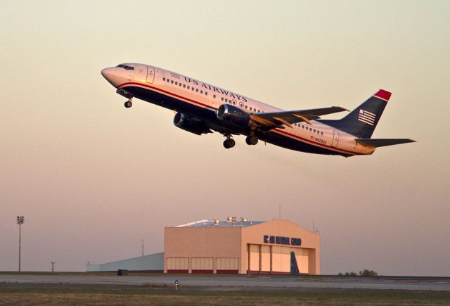 BOEING 737-400 (N423US) - Evening takeoff with the North Carolina National Guard hangar in the background. The landing gear are just beginning to close as the aircraft climbs into the fading evening sky.