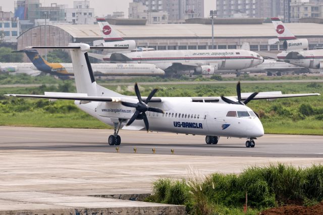de Havilland Dash 8-400 (S2-AGW) - 7th Oct., 2015. US-Banglas "Albino", as she is affectionately known to Bangladeshi spotters, rolls on to runway 14 for departure.  Background shows the ever aging "graveyard" at Zia International Airport in Dhaka.