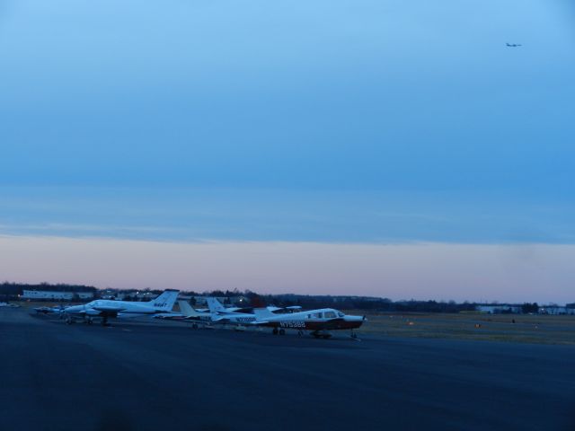 Piper Cherokee (N75382) - Planes Parked On One Of The Ramps At KHEF While The Sunset Turns Clouds Pink, At The Same Time N969FD, A FedEx Boeing B757-200F Package Freighter, Approaches Dulles International Airport On The Top Right