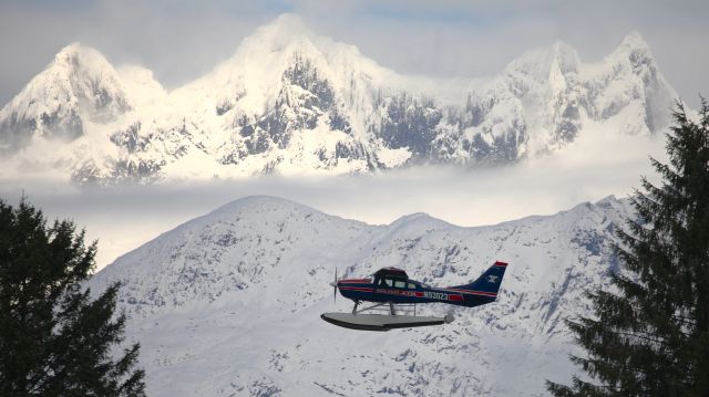 Cessna 206 Stationair (N93023) - N93023 just after takeoff at PAJN's float pond.  I could hear the engine through the trees and was waiting for him to come into view.  The Mendenhall Towers in the background caught some sun through a gap in the clouds.