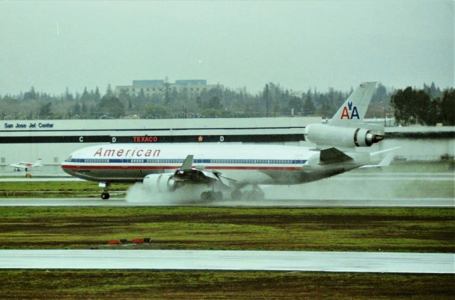 Boeing MD-11 (N17XX) - KSJC - early 1990s at San Jose CA USA rain meant 12R arrivals, so I'd race up to the top floor of the parking lot and wait for the 0900am ish arrival of the Narita NRT-San Jose SJC MD-11 to land - I don't have the reg here on posting but I filmed the taxi back  on video - finding that segment of my 500+ videos will take awhile. San Jose Airport officials ruined this view several years later building the new US Customs building at the south end of Terminal A, pretty much right in this view,,,and eventually screwing up the whole view forever building the Gawd awful looking Terminal C. to the left of this view many years later. SJC Airport officials knew there was a dedicated airline photography group at SJC and we even lobbied for a view platform - they seemed interested during meetings but then, "Nah - " which is why I post what I do.
