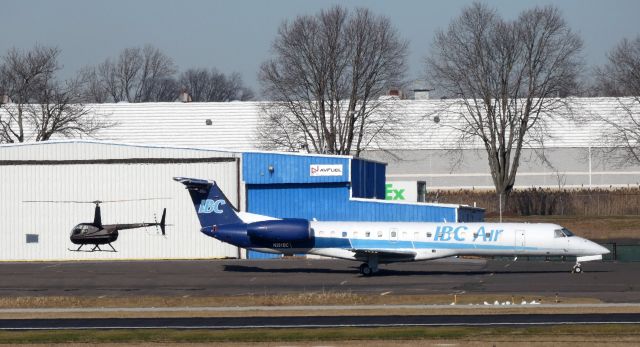 Embraer ERJ-145 (N261BC) - Catching some Tarmac time is this 1998 Embraer 145EP while a Robinson R44 Rotorcraft passes aft of the Twin Engine Jet in the Winter of 2020.