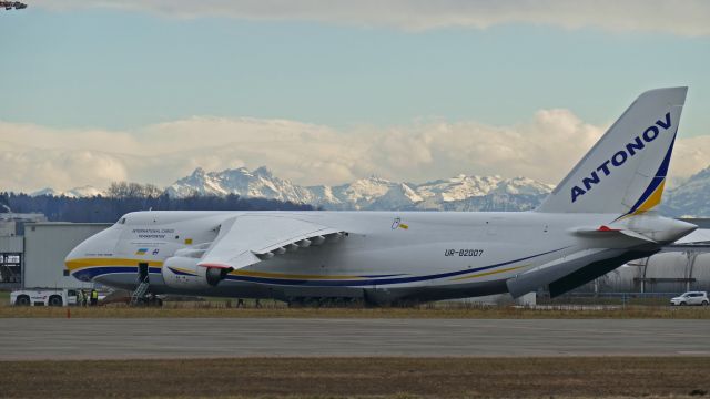 Antonov An-12 (UR-82007) - Tractor tows the cargo plane towards taxiing in front of the beautiful illuminated Swiss alps.