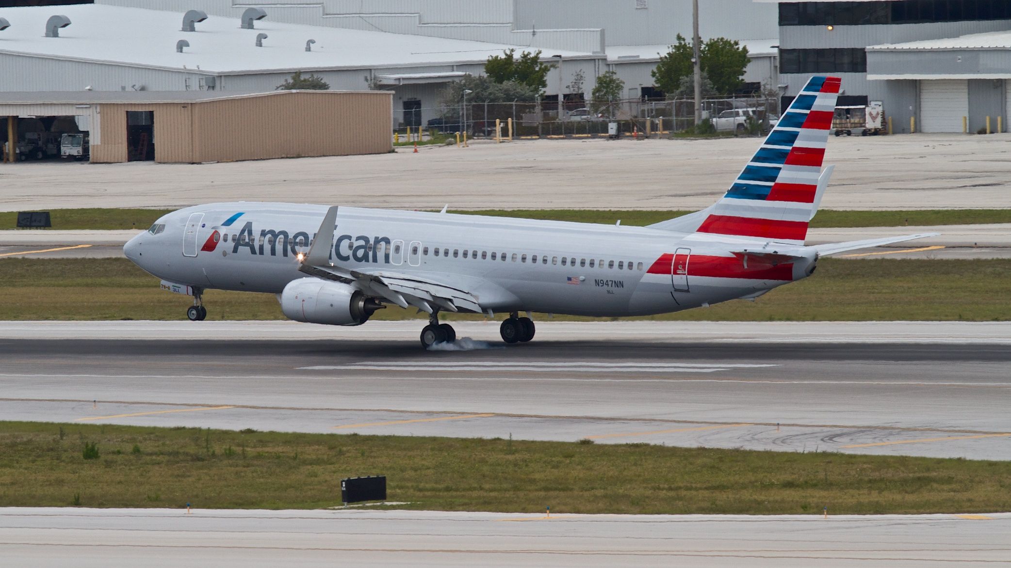 Boeing 737-800 (N947NN) - The exact moment of left main gear contact with Runway 28R (right main is still a few inches off the ground).