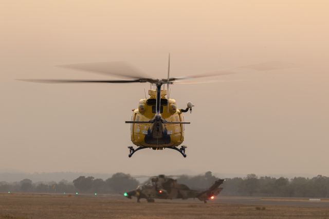 Bell 412 (VH-EPR) - This aircraft always backs out and does a 270-degree turn to the right before exiting the helipad area.  That's a Eurocopter Tiger ARH preparing to leave also.  This was shot just after the sun set and the bushfire smoke is smothering the light.