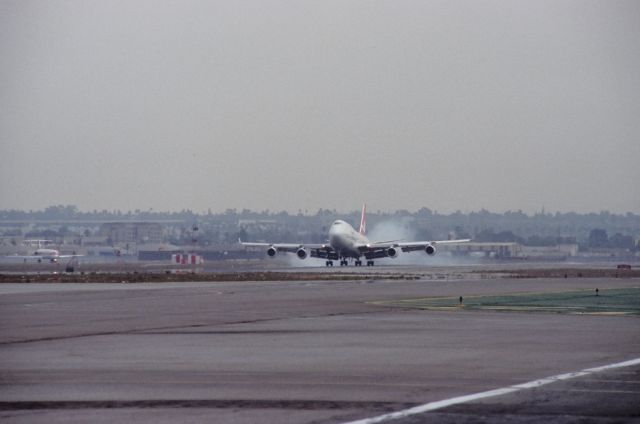 Boeing 747-400 (VH-OJE) - KLAX - March 1990 not my best photo but this shows VH-OJE smoking 25L arriving from Sydney - the view shows what it used to be like filming from the old Imperial terminal parking lot back in the day. One used to be able to sit here all day and photograph airliners arriving by the minute. The fence used to be about 6ft tall, small barbed wire and ladders were allowed as long as kept back from the fence - before 911 attcks, was about 1 ft back. I used a small pick up truck and I had a 8ft ladder in the back - I can imagine what the digital days would produce if this lot was still open, This photo was a Minolta XD-11 and a 60-300mm lens and color negative converted to a CD, and a crummy job by Costco as it is. TV