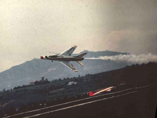 — — - USAF Thunderbirds F-100 Super Sabre performing at Rimini Miramare Airport (Italy) during the spring or summer of 1967. Photo is from a color slide taken by my father while he was stationed at Rimini Airbase with the Detachment 2700 7232nd Munitions Maintenance Group and with the Italian 5A Aerobrigata. A tower of San Marino is visible on the mountain in the distance just above the vertical stabilizer. 