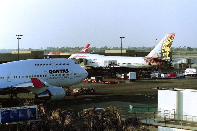 Boeing 747-400 (VH-OED) - KLAX - Jan 1998 - jet weekend and photo run at Los Angeles from the SJC area with Mike and Mark Durbin and Craig Curtis - late PM near the TBT - QANTAS -OED on the push back as G-BNLZ is serviced after arriving from LHR. "Wunala Dreaming" also being towed to remote in the background. After 911 Terror attacks, this view was blocked from the upper parking garage.....