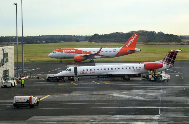 Embraer ERJ-145 (G-SAJF) - Loganair - Embraer ERJ-145EP (G-SAJF) on "stand" at NCL with easyJet - A320-214WL (OE-IJI) taxiing for "take off" in the background. Photo taken from inside NCL's "International Departures". (Photo 16 Oct 23)