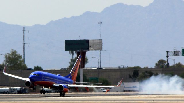 Boeing 737-700 (N236WN) - Hot and Hotter: Southwest N236WN recovers after a terrific bounce on the hot Phoenix runway (see smoke). Note the direction of the windsock under the port wing. This was the last landing on 7R before the runway changed direction. Photo taken 2012-08-05 13:08 MST.