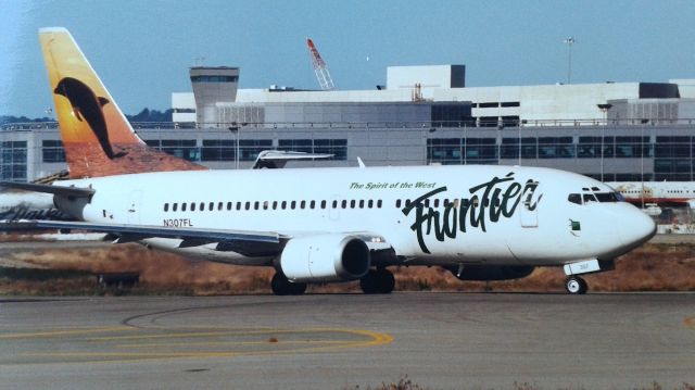 BOEING 737-300 (N307FL) - KSFO - "Flipper" - Frontier Airlines 737-300 rolling to Runway 1R between Jan 2000 and Sept 2001 from the Millbrae Airpark, Note the "Ahoy Tower" in the background at the new Intl terminal which if memory is correct - opened Dec 2000. Millbrae Airpark was closed Sept 11th, 2001.