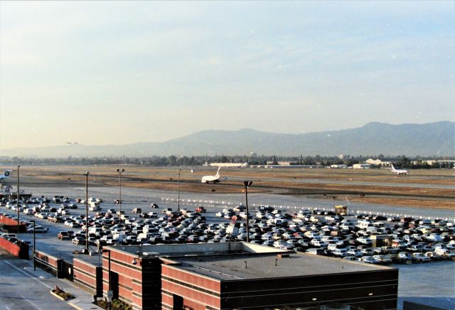 Boeing 737-200 (N245WA) - KSJC - in the late 1980s, when San Jose Airport was ready to build the new Terminal A, there was a long term parking lot spread north and south from under where I took this photo now, atop the new terminal A garage. To make additional parking spaces, SJ Officials made a good choice in my favor, and allowed public parking down in the lot shown here, open to the public, out on the ramp!!!! .( Shown here, it was reverted back to employees only parking after the A garage was built) Fine by me, I took the view over being close up, at this point. But I did get plenty of video and photos from the lot shown here parked up by he fence, was never hassled by Airport cops, but they did drive by and look at me standing on the 8ft ladder in the back o f my 4wd pickup...yes, weird looks! I always waved at them and they'd take off. Shown here is Delta N245WA on taxi to the C terminal as a US Air 737-300 departs Runway 30L with a DC-8 smoking up his tail side - one of the closest approaches and take off at San Jose I had ever seen. I have other photos but thought the boring parking lot story would be better!