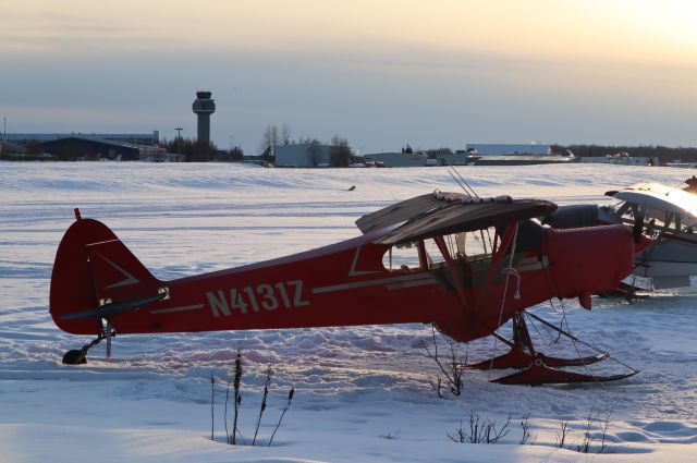 Piper L-21 Super Cub (N4131Z) - Super cub on skis on Lake Hood ice at springtime sunset.  Anchorage International airport tower in background.