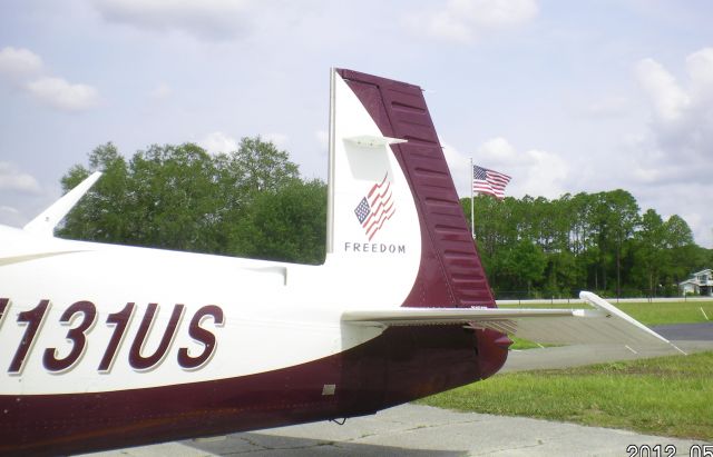 Mooney M-20 Turbo (N131US) - N131US sports a Freedom logo on the tail.  In background is the flag pole at Spruce Creek Airpark, Florida (7FL6).