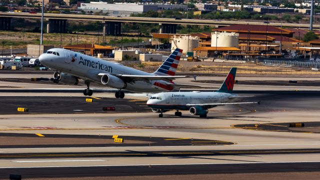 Airbus A319 (N838AW) - American Airlines A320 taking off from PHX on 8/20/22 while an American Airlines A319 in America West retro livery taxis in the background. Taken with a Canon 850D and Rokinon 135mm f/2 manual focus lens.