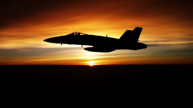 — — - An F-18 in the sunset.