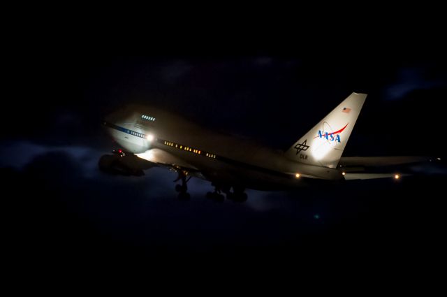 BOEING 747SP (N747NA) - NASA's one-and-only 'Sophia' B747-SP (callsign NASA-747) flying infrared telescope observatory lifting off Runway-20 tonight at Christchurch International Airport for a night flight over the Southern Ocean south of New Zealand. I quickly shot over to the airport after work with my camera gear to see her depart on her latest mission over New Zealand. I heard the crew on 'Ground' so got ready near the runway intersection outside the fire rescue station. ATC had a Dash-8 on short final popping out of the soup about 8 miles downwind with a request to slow down to minimum approach speed so as to let Sophia get airborne. This photo as can be seen, was shot in the dark with ISO at 6400, 1/45s, f2.8 at 160mm. Processed lightly in Lightroom to get rid of the noise.