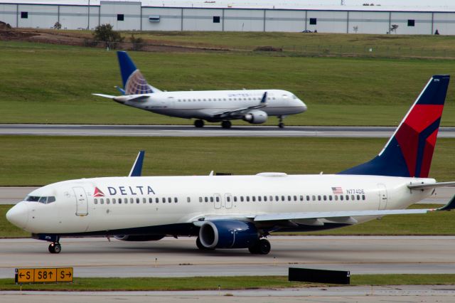 Boeing 737-800 (N774DE) - A Delta 737 taxiing to 18L, while a United ERJ takes off in the background.