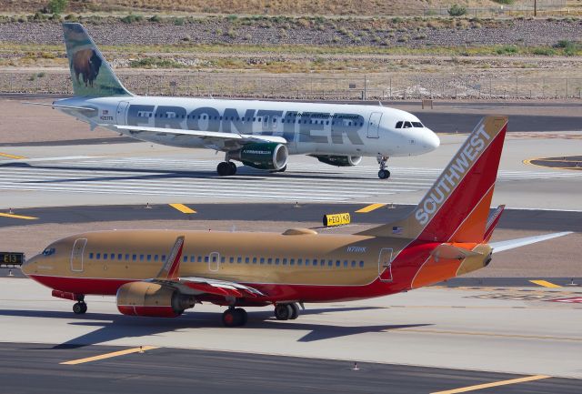 Airbus A320 (N207FR) - Frontier A320 taking the runway to depart while Southwest's "Herbert D. Kelleher" N711HK retro taxis out for departure (View in "full" for highest image quality)